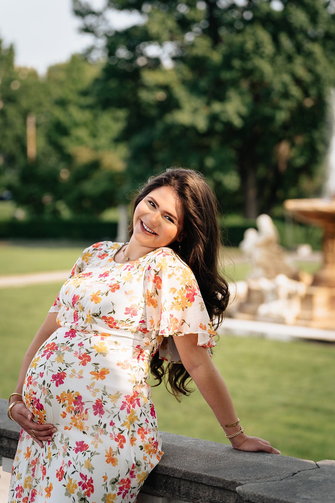 Hala smiling with a hand under her bump, the Fountain of the Waters and museum lawn behind her
