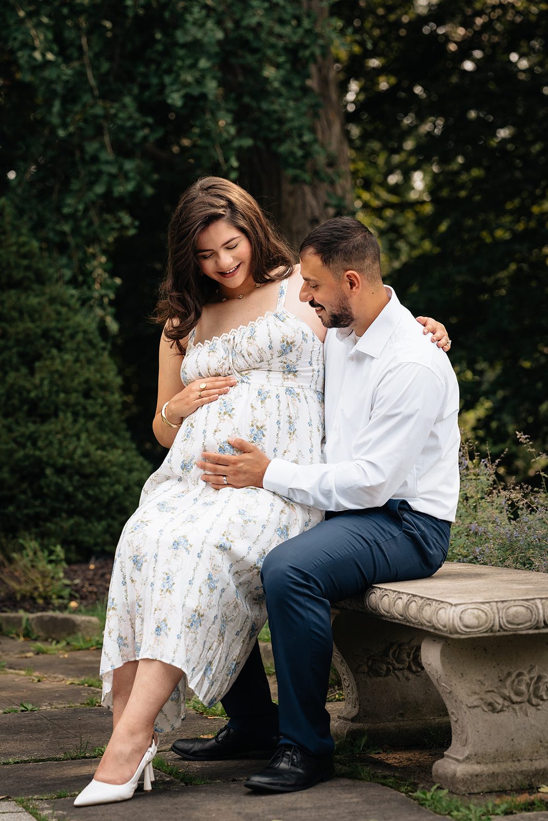Hala seated on Abe's lap on a stone garden bench surrounded by dense green foliage