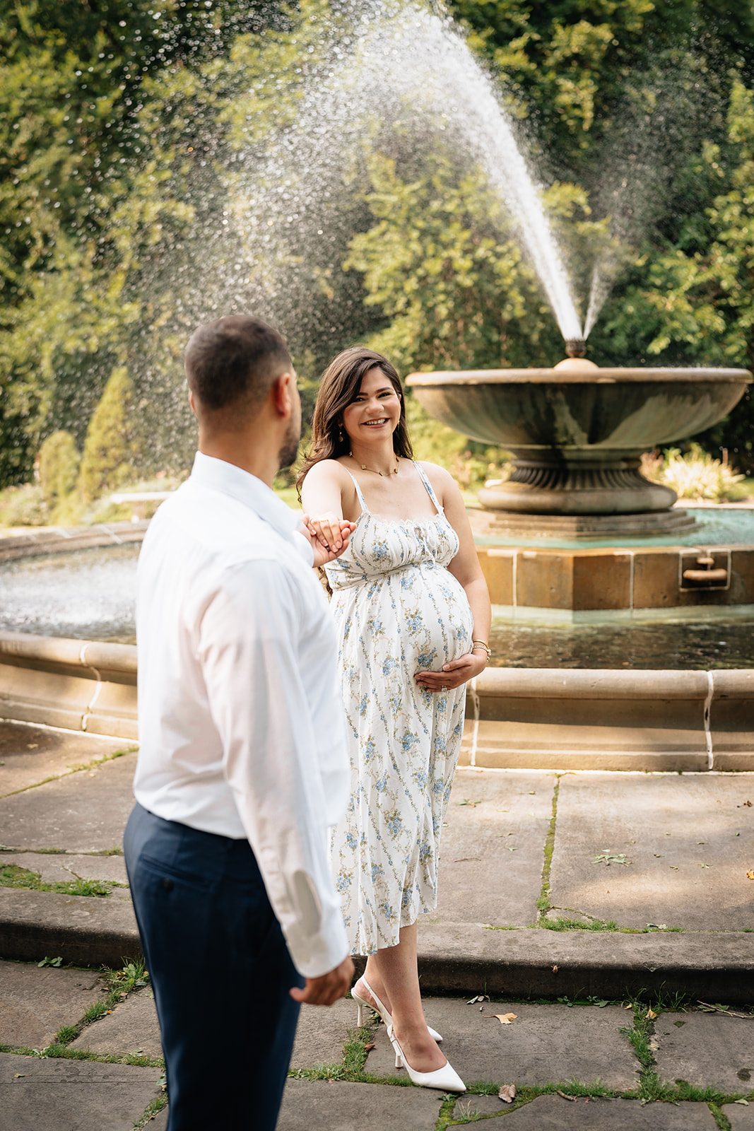 Wide frame of Hala and Abe standing together beside the tiered fountain in the Italian Cultural Gardens