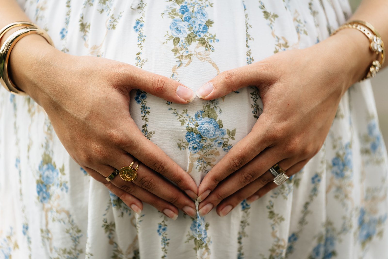 Close detail of Hala's hands framing her bump over the blue floral fabric of her dress