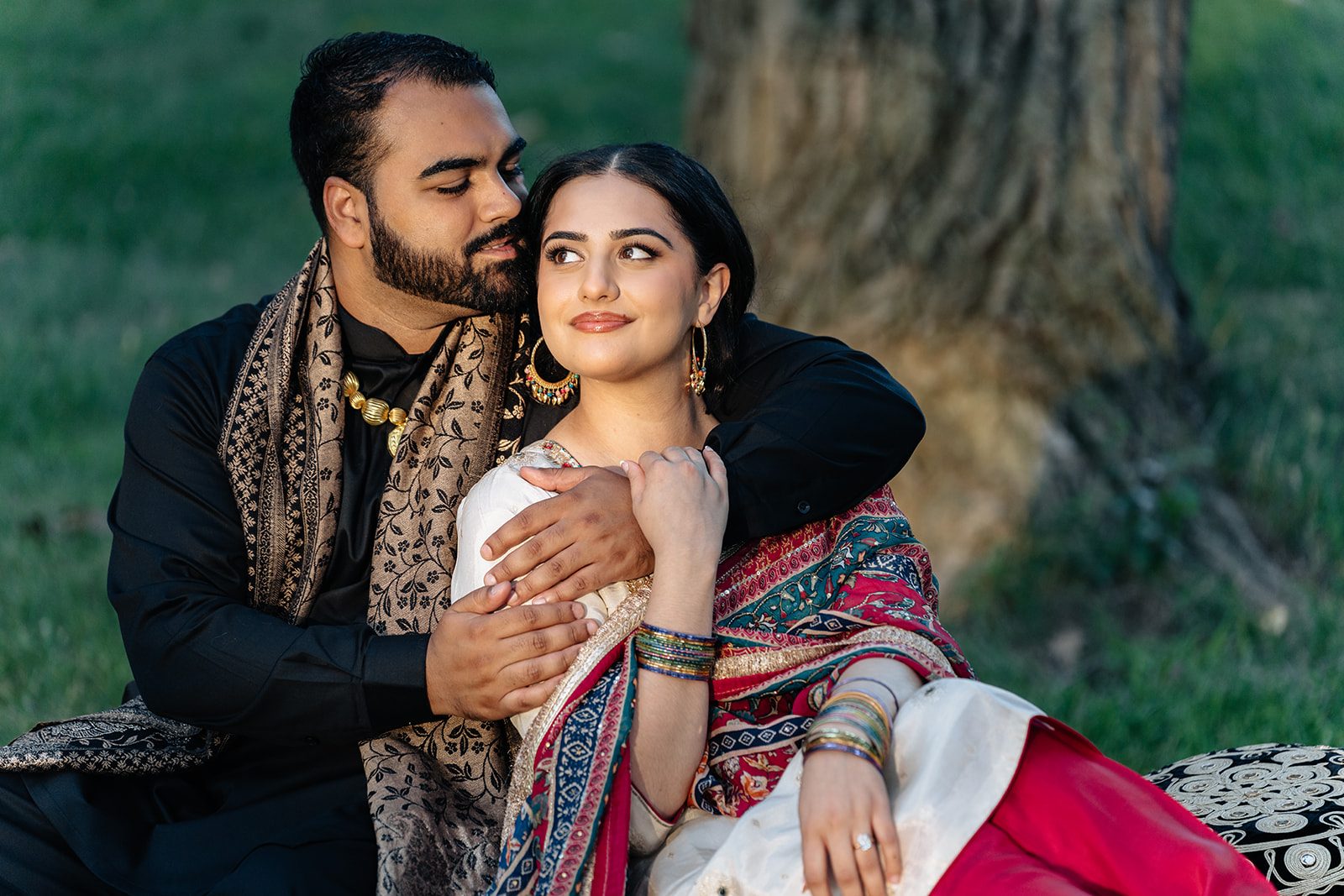 Harry cradling Ramneet beneath a large tree trunk in a second outfit, a calm editorial mood