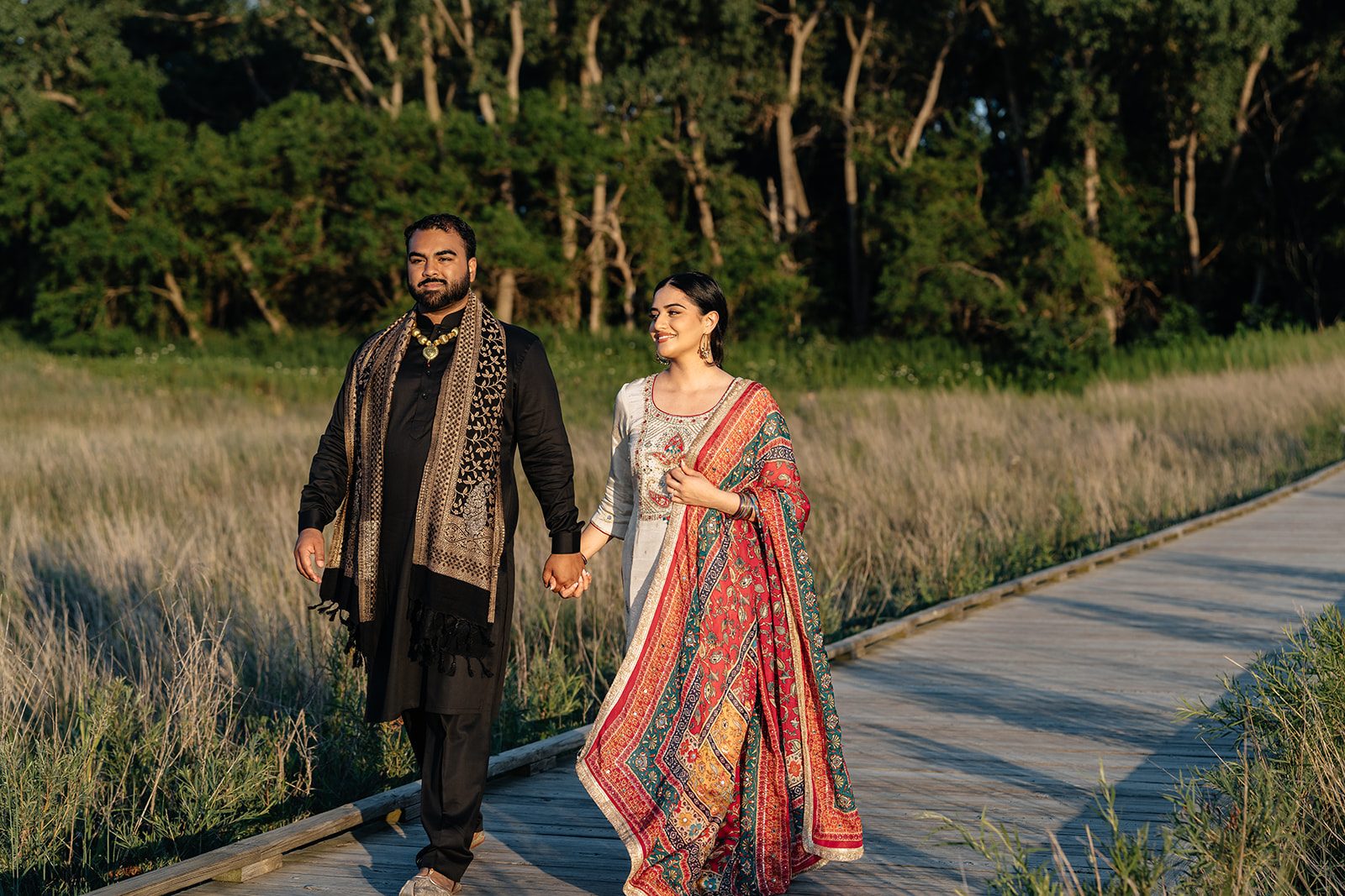 Couple walking hand in hand along the wooden boardwalk in golden light, mid-stride and laughing
