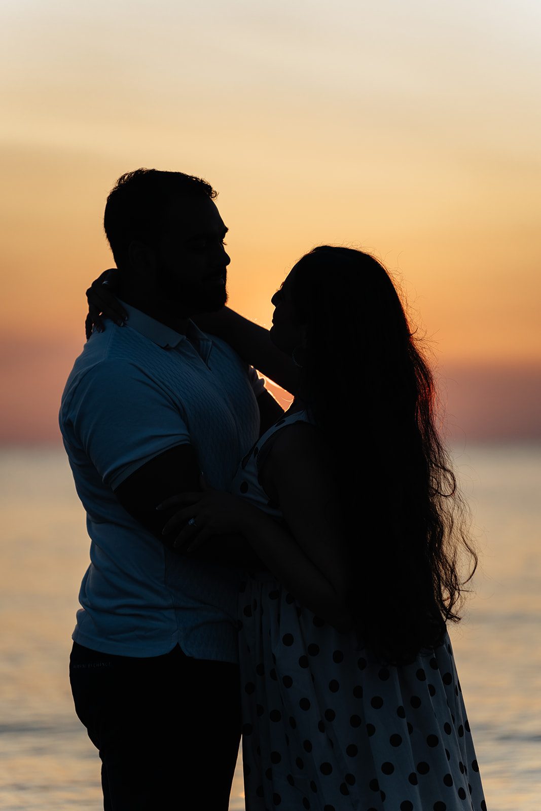 Sunset silhouette of the couple with their faces nearly touching against a warm gradient sky