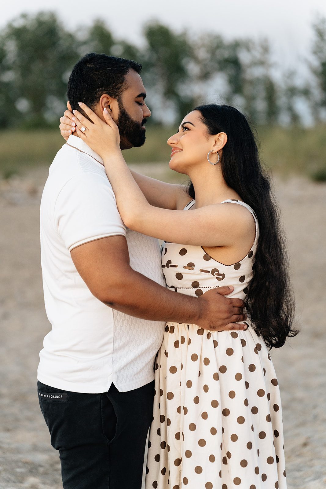 Ramneet holding Harry's face in her hands in a casual look with the beach and treeline soft behind them