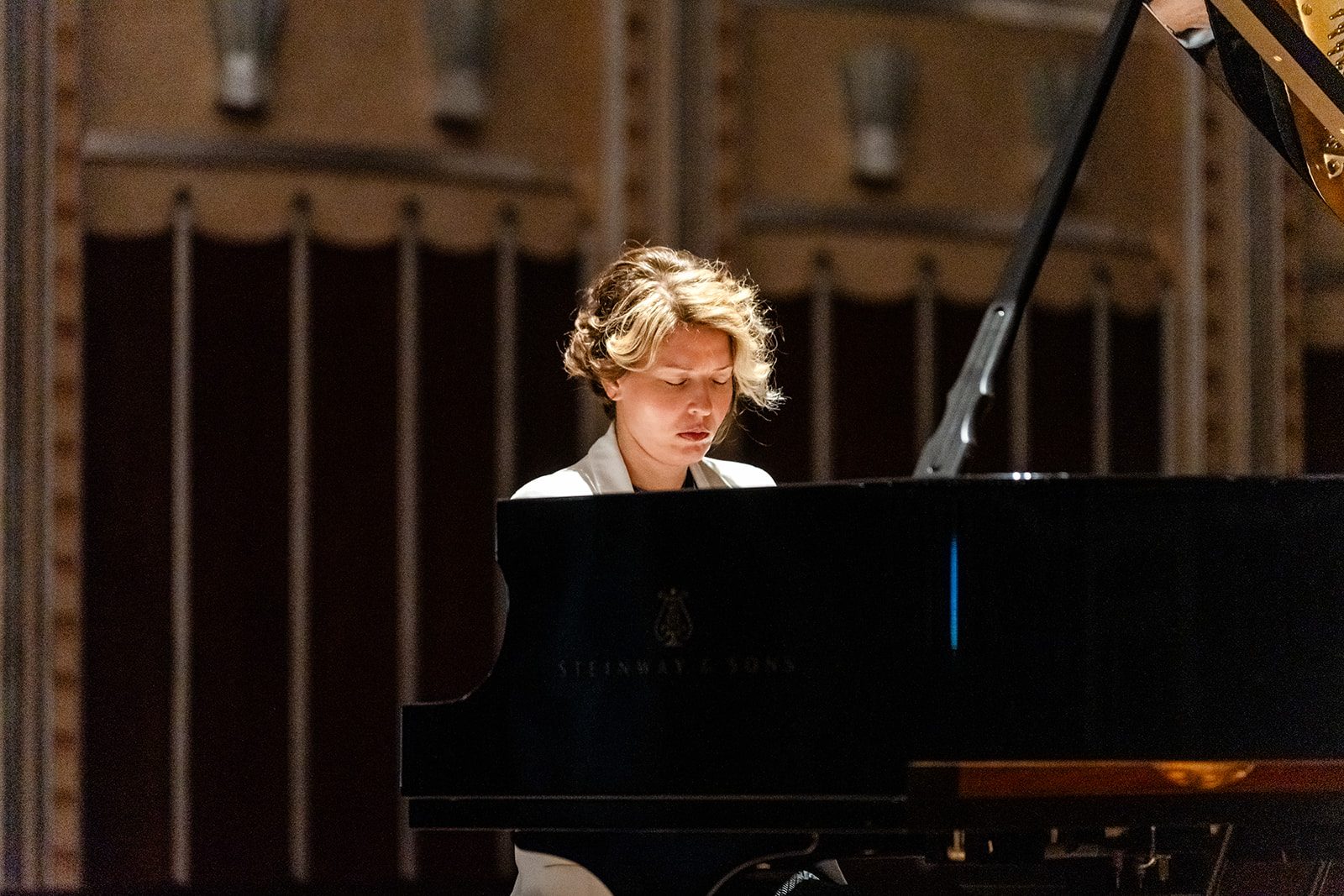 Tight expressive portrait over the Steinway lid, white blazer, eyes closed mid-phrase during the Cleveland recital