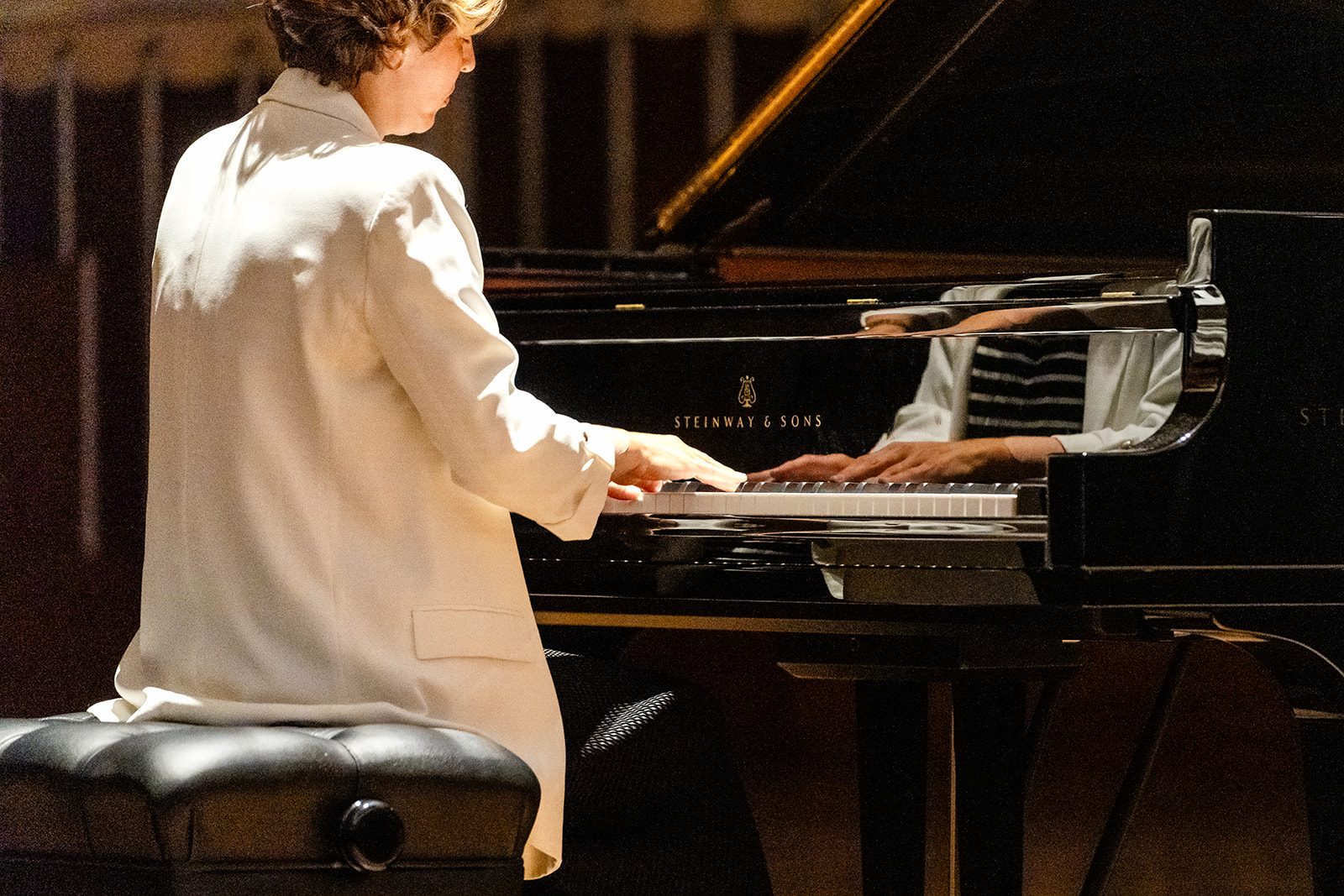Over-shoulder view of both hands on the keys with STEINWAY & SONS lettering visible and a reflection in the polished fallboard