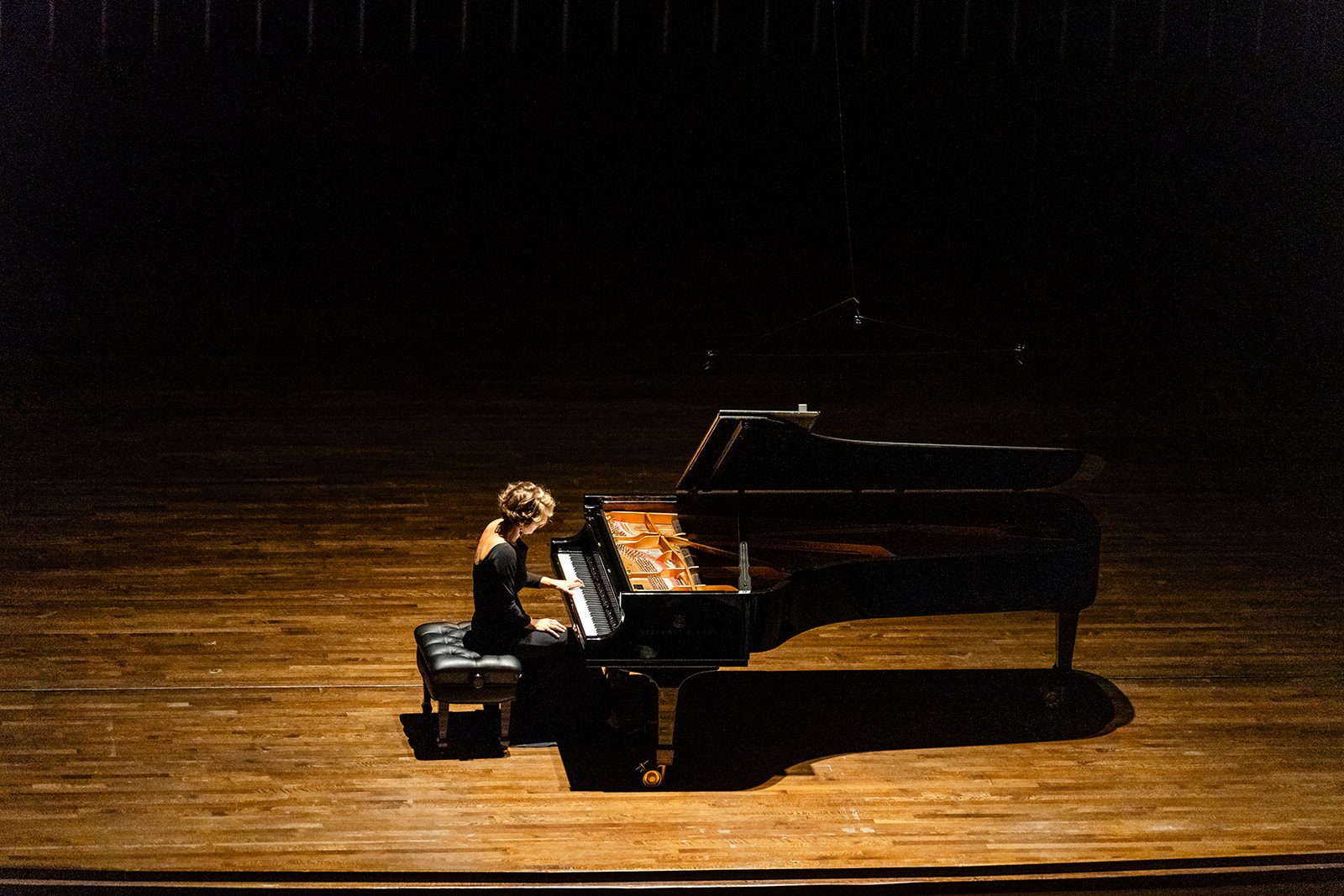 Elevated minimalist stage composition with the pianist and piano isolated against black and strong negative space