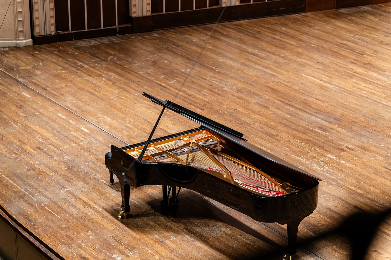 Overhead detail of the open Steinway showing strings and the gold plate against the warm wood stage