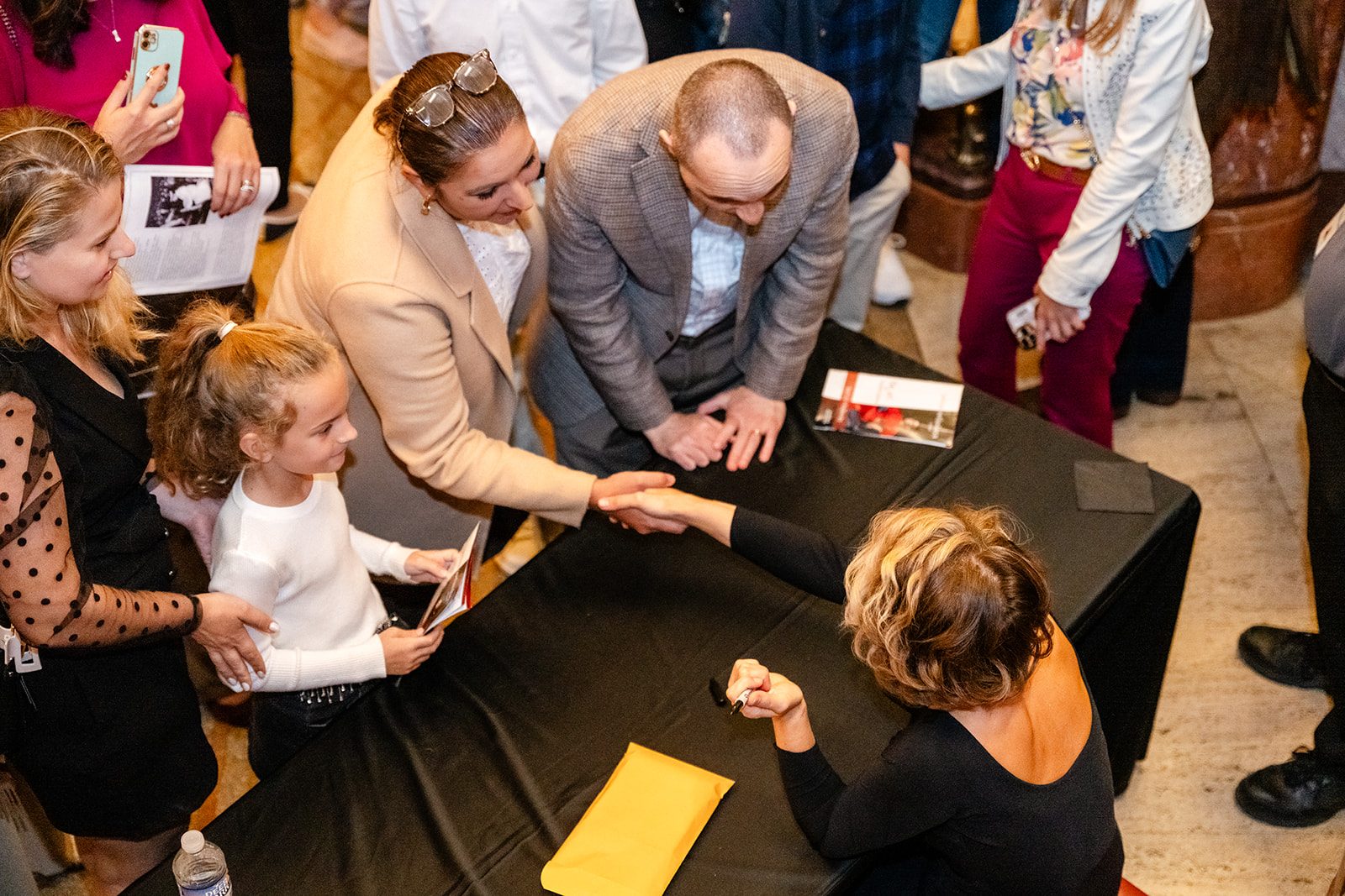 Overhead human-connection frame during a handshake in the lobby with family and a child nearby