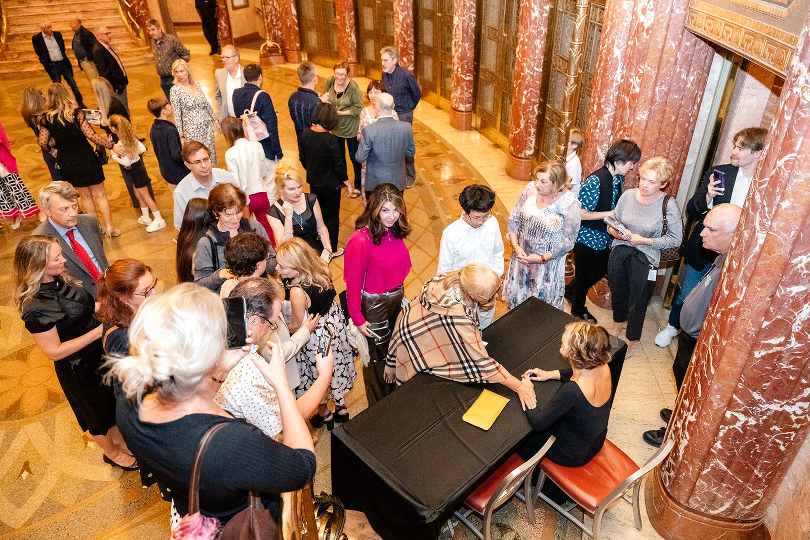 Overhead wide of the Severance lobby crowd queued around the signing table beneath the ornate interior